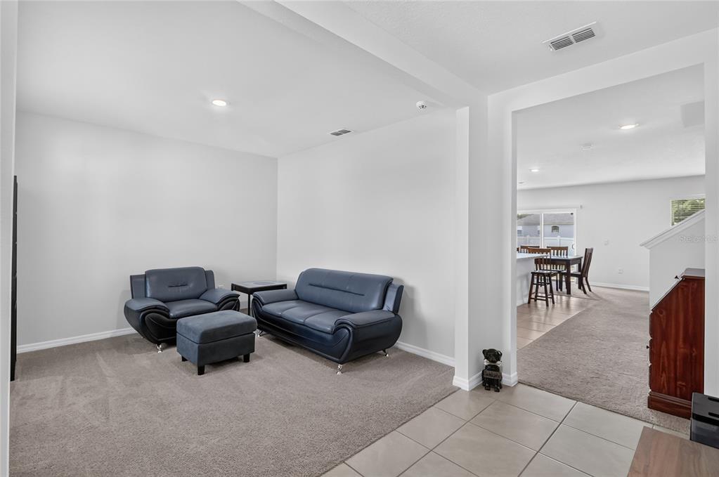 A carpeted living room with dark blue leather furniture opens into a tiled dining area — 787 AUBURN GROVE CT., AUBURNDALE, FL