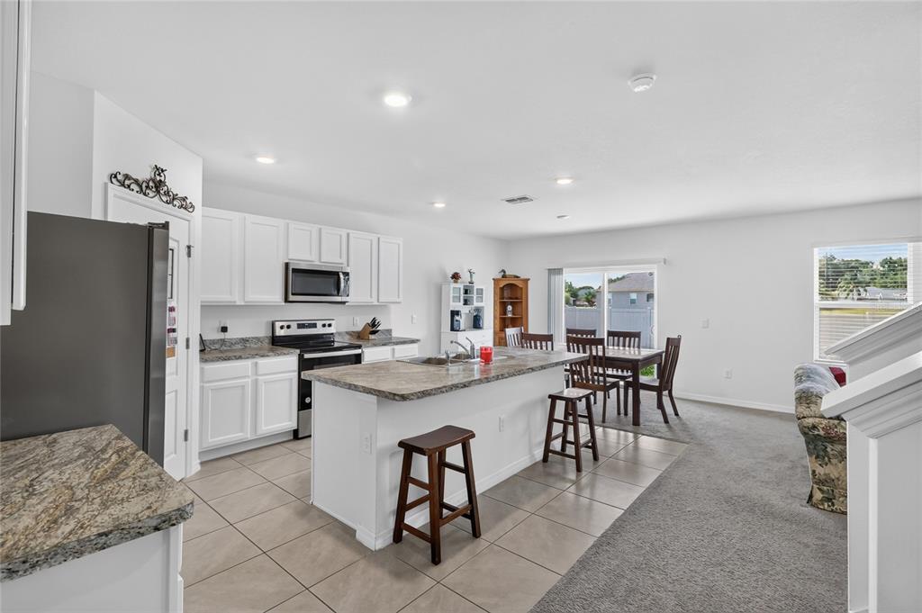 A kitchen with white cabinets, granite countertops, and an island with stools, adjacent to dining — 787 AUBURN GROVE CT., AUBURNDALE, FL