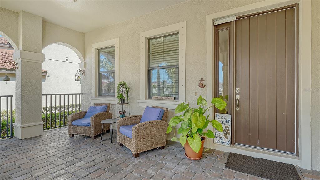 A covered front porch features a brick paver floor, two wicker chairs, and a wooden door — 5723 TITLE ROW DRIVE, BRADENTON, FL