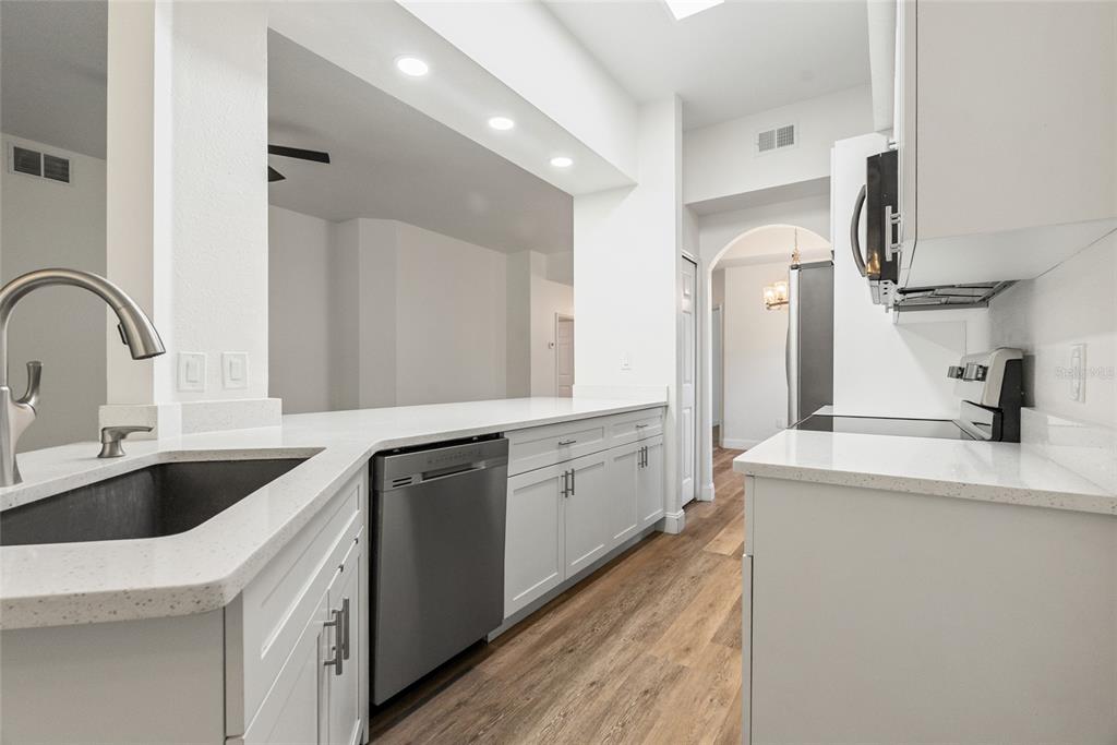 A hallway with wood-look flooring leads to a bathroom featuring a dark vanity and mirror — 9416 MYRTLE CREEK LANE UNIT 701, ORLANDO, FL
