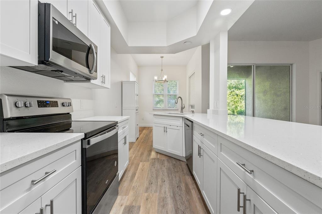 A view from a hallway into an open-concept living area with wood-look flooring and kitchen — 9416 MYRTLE CREEK LANE UNIT 701, ORLANDO, FL