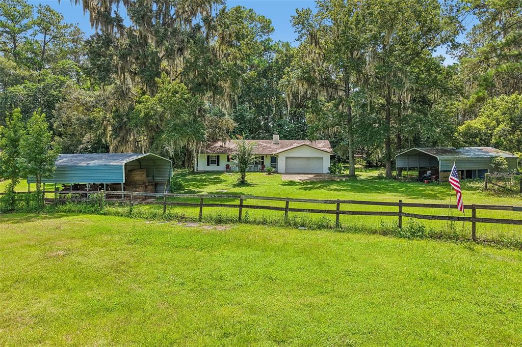 A single-story house with a garage sits on a grassy lot between two metal carports — 5230 NW 144TH PLACE, REDDICK, FL