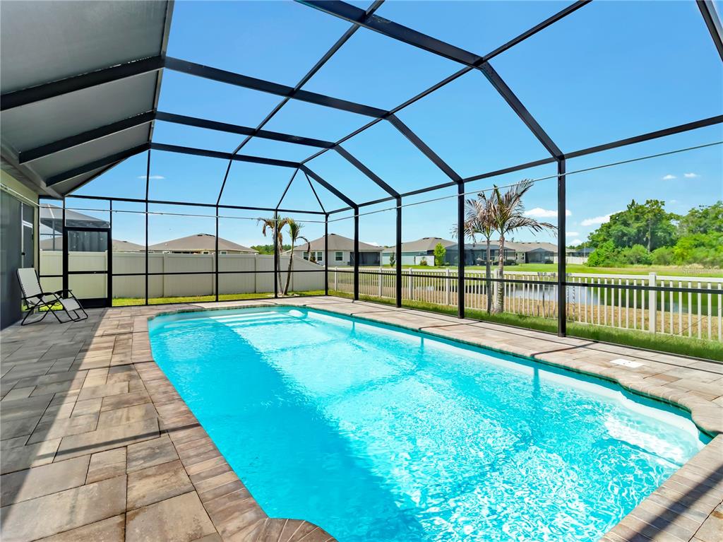 A screened-in swimming pool with a paver deck overlooks a pond and neighboring houses — 5063 IVORY STONE DRIVE, WIMAUMA, FL