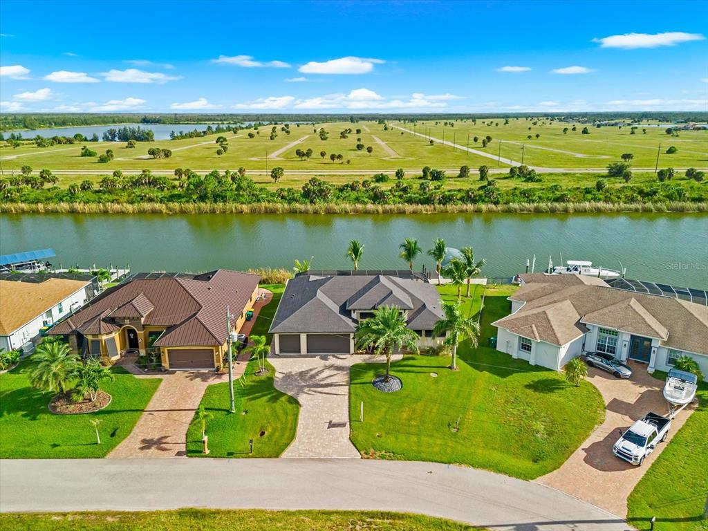 An aerial view shows three suburban houses along a canal with a large field beyond — 10572 RAINSVILLE STREET, PORT CHARLOTTE, FL