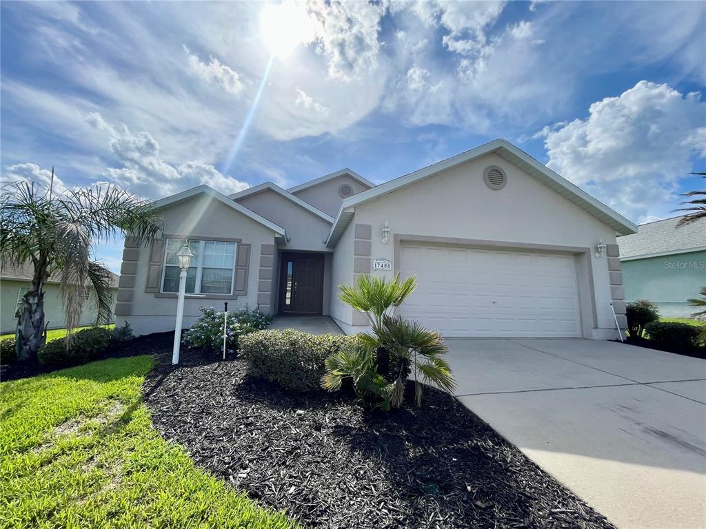 A single-story house with a beige stucco exterior, a two-car garage, and a landscaped yard — 17408 SE 121ST CIRCLE, SUMMERFIELD, FL
