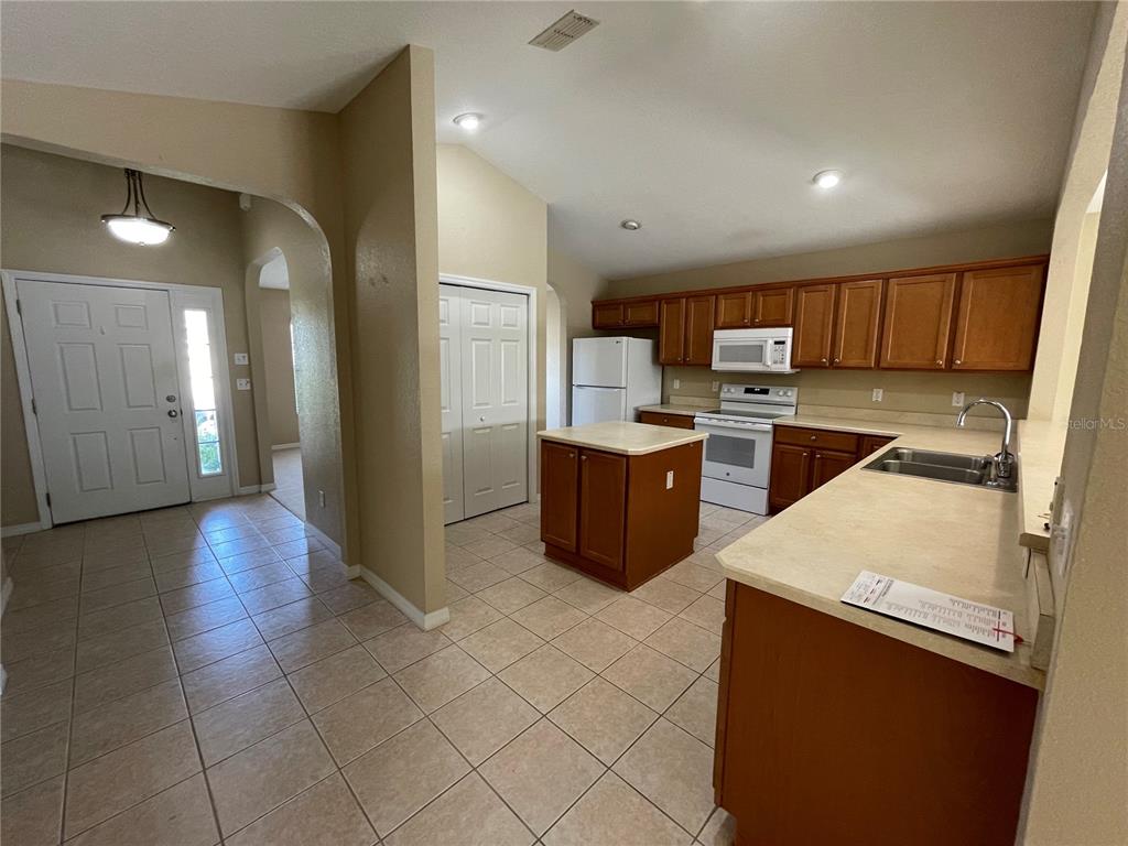 A kitchen with wood cabinets, a center island, and tile flooring opens to an entryway — 17408 SE 121ST CIRCLE, SUMMERFIELD, FL