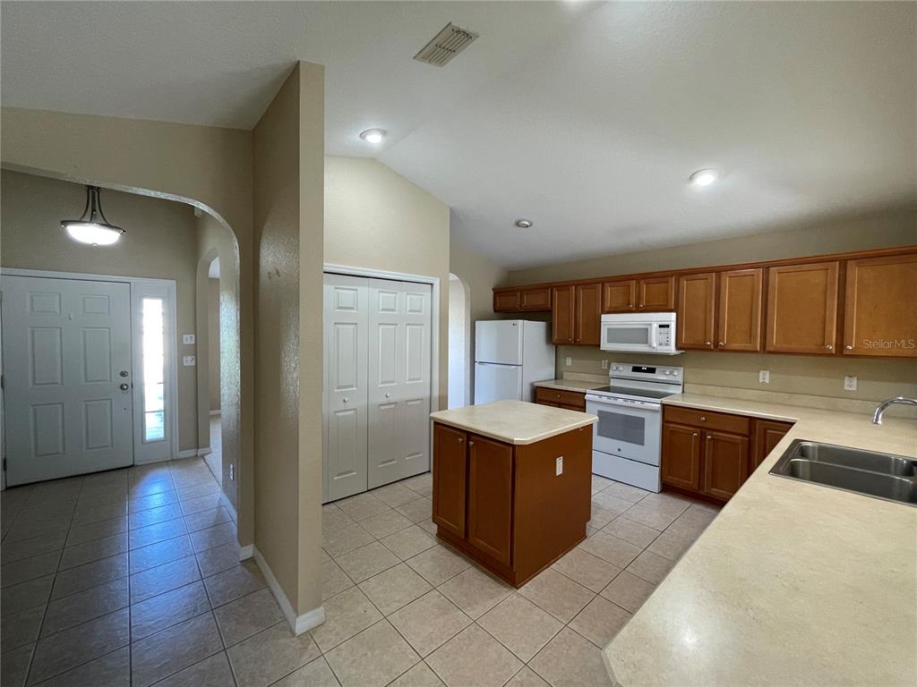 A kitchen with wood cabinets, white appliances, a center island, and tiled flooring — 17408 SE 121ST CIRCLE, SUMMERFIELD, FL