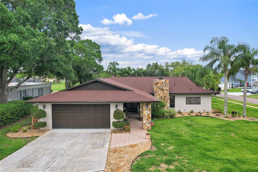 A single-story house with a brown roof, stone chimney, and attached garage sits on a lawn — 10 ARBOR LANE, OLDSMAR, FL