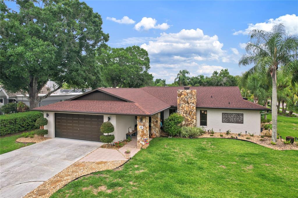 A single-story house with a brown roof, stone chimney, and attached garage sits on grass — 10 ARBOR LANE, OLDSMAR, FL
