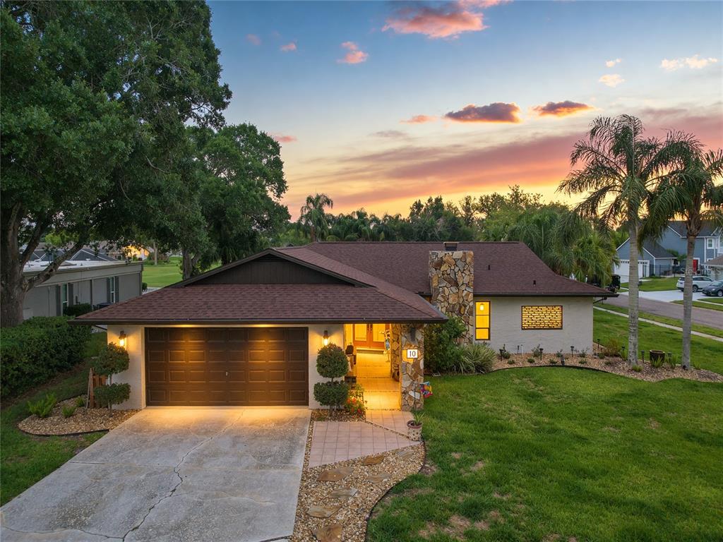 A single-story house with a stone chimney, brown roof, and attached garage at sunset — 10 ARBOR LANE, OLDSMAR, FL
