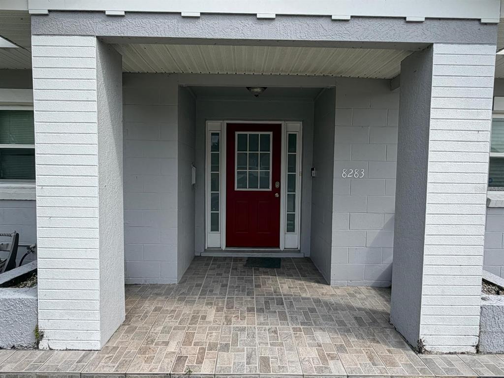 A red front door with sidelights is centered under a covered porch with tiled flooring — 8283 LE MESA STREET, ORLANDO, FL