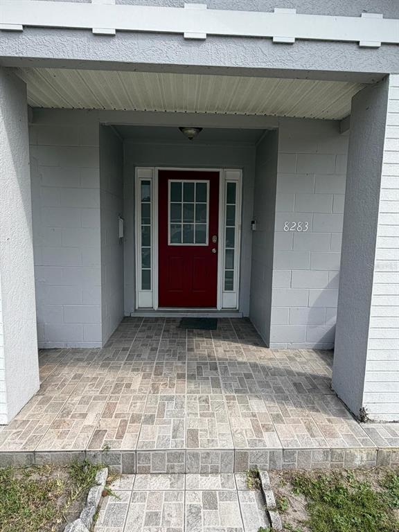 A red front door with sidelights is centered on a tiled porch with gray walls — 8283 LE MESA STREET, ORLANDO, FL