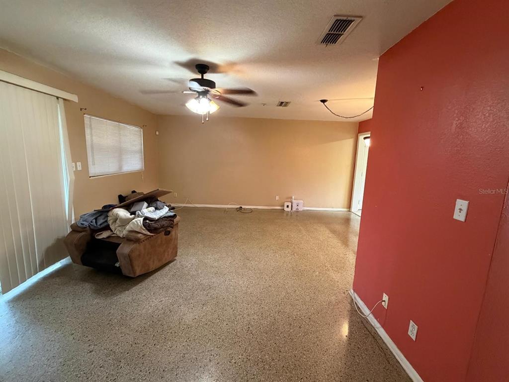 A living room features tan walls, a red accent wall, and speckled concrete flooring — 8283 LE MESA STREET, ORLANDO, FL