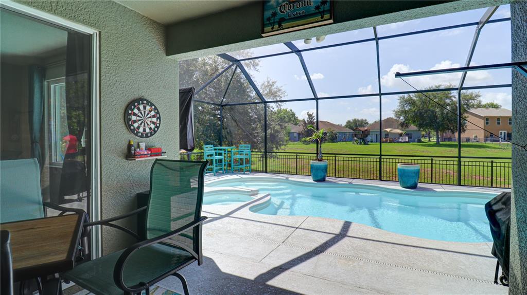 A covered patio features a dartboard, outdoor furniture, and a screened-in swimming pool — 5725 JUSTICIA LOOP, LAND O LAKES, FL