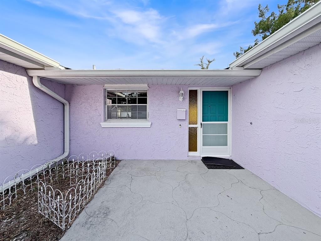 The exterior of a house features lavender stucco walls, a concrete patio, and a teal door — 3 HERITAGE COVE COURT, CASSELBERRY, FL