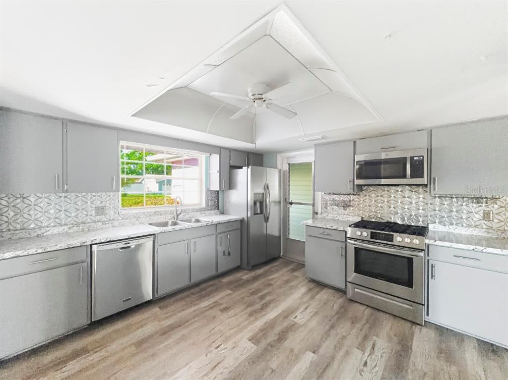 A kitchen features gray cabinets, stainless steel appliances, patterned backsplash, and a tray ceiling — 3 HERITAGE COVE COURT, CASSELBERRY, FL