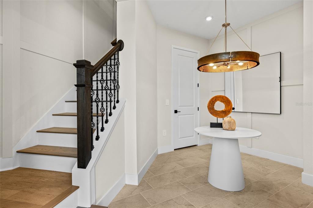 A foyer features a white pedestal table, a modern chandelier, and a wooden staircase — 12807 JADE EMPRESS LOOP UNIT 201, VENICE, FL