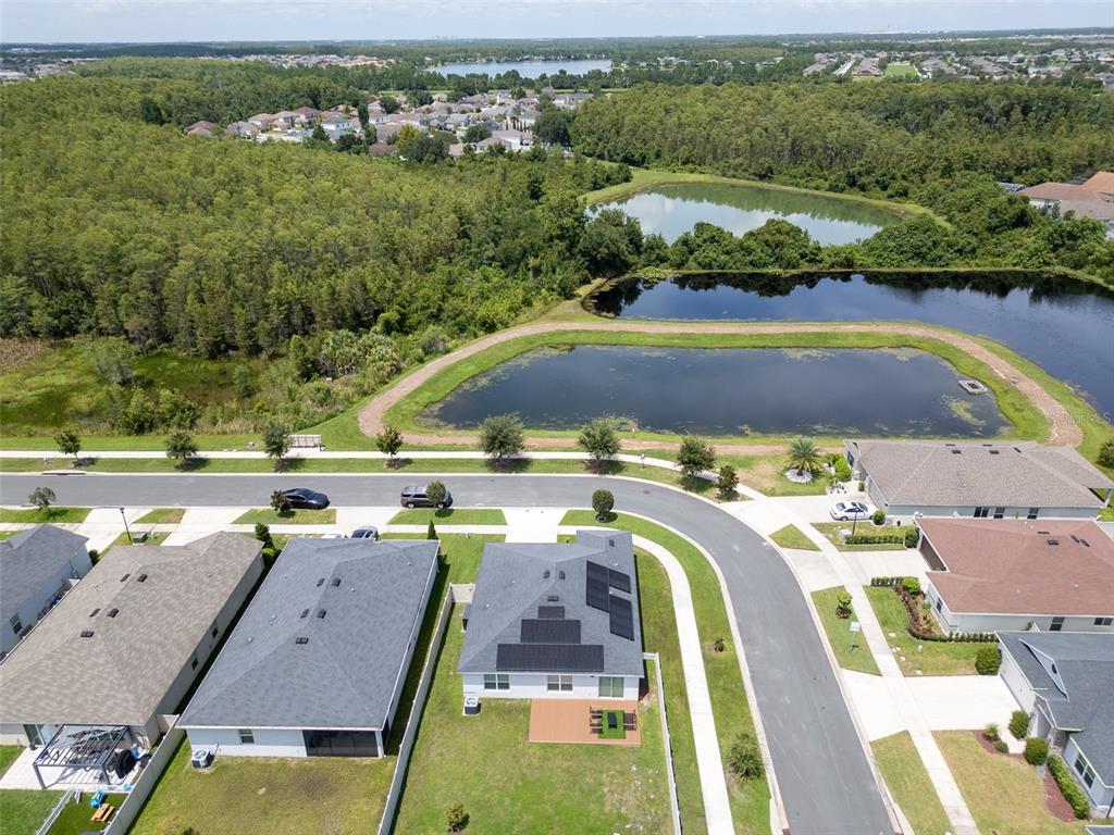 An aerial view shows a suburban house with solar panels near ponds and wooded areas — 3122 EAGLE HAMMOCK CIRCLE, KISSIMMEE, FL