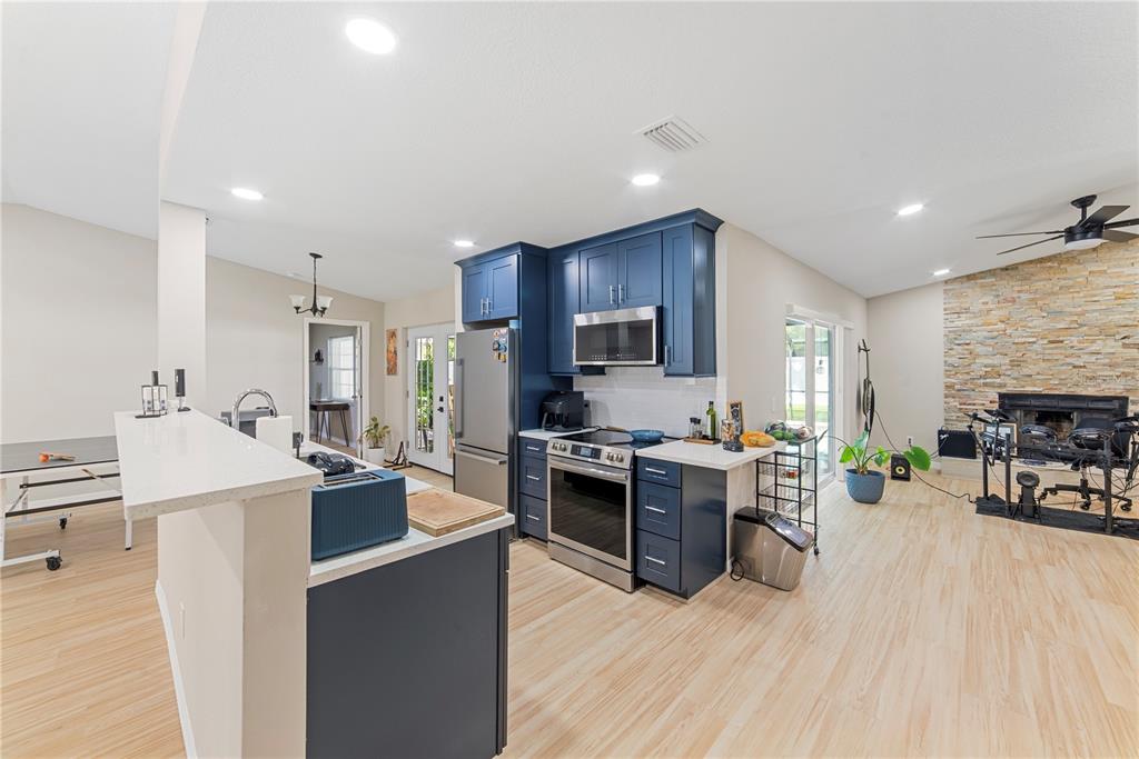 A kitchen features blue cabinets, stainless steel appliances, and a stone fireplace in the living area — 1003 RED OAK CIRCLE, BRANDON, FL