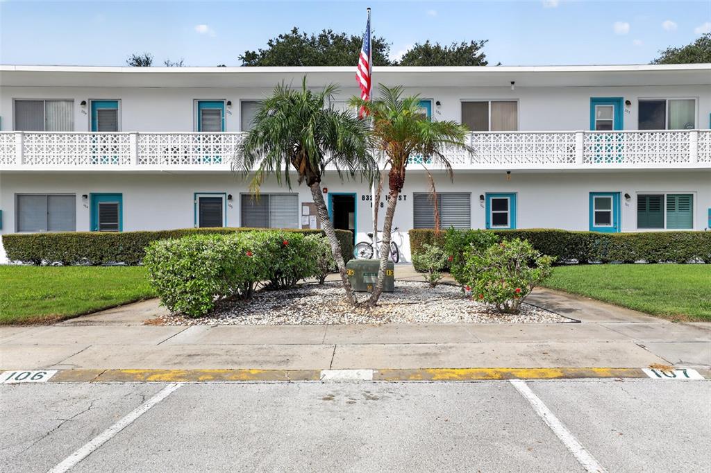 A two-story apartment building features white exterior walls, blue door frames, and a central palm tree — 8320 112TH STREET UNIT 208, SEMINOLE, FL