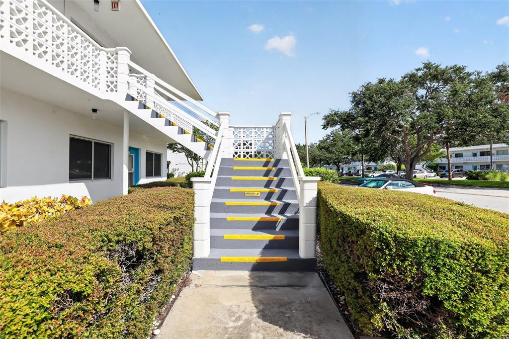 An outdoor staircase with yellow-striped steps leads to a second-floor balcony of a white building — 8320 112TH STREET UNIT 208, SEMINOLE, FL
