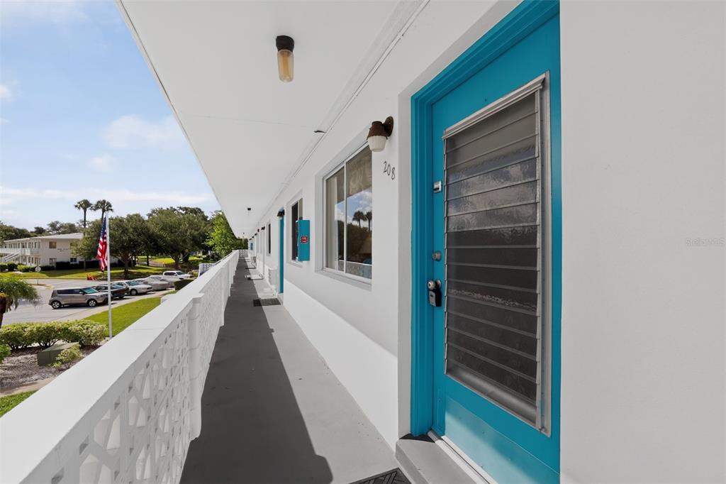 An outdoor balcony walkway features white walls, a bright blue door, and a lattice railing — 8320 112TH STREET UNIT 208, SEMINOLE, FL