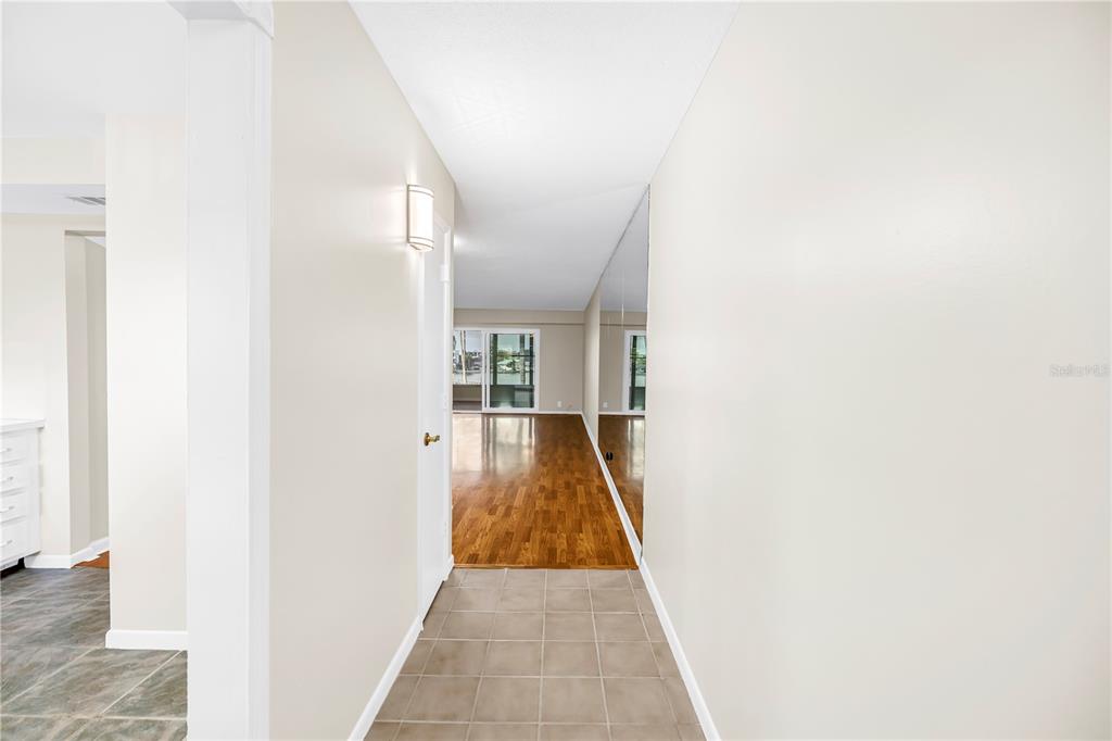 A hallway with tiled flooring leads to a living area featuring hardwood floors and mirrors — 1868 SHORE DRIVE S UNIT 310, SOUTH PASADENA, FL