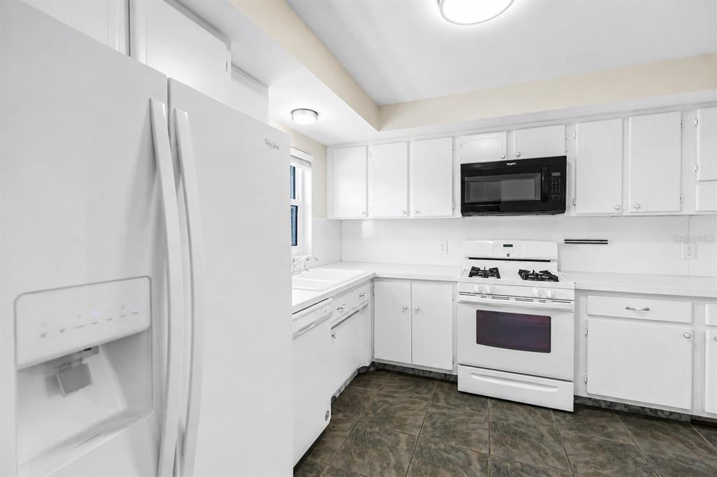 A white kitchen features white cabinetry, white appliances, and dark tile flooring — 1868 SHORE DRIVE S UNIT 310, SOUTH PASADENA, FL