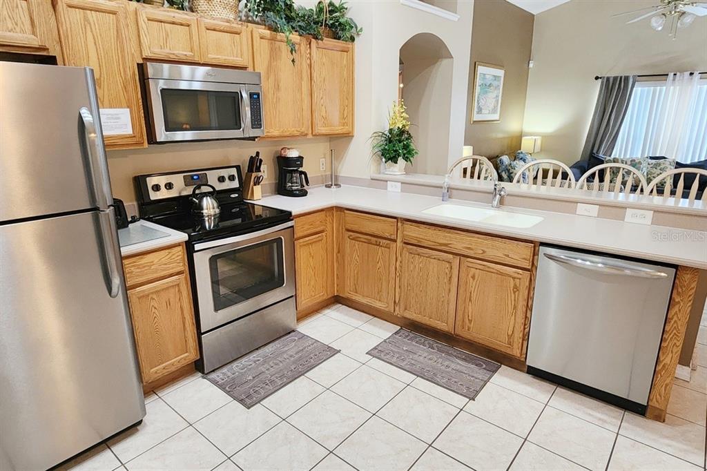 A kitchen with oak cabinets and stainless steel appliances opens to a living room area — 2914 BLOOMING ALAMANDA LOOP, KISSIMMEE, FL
