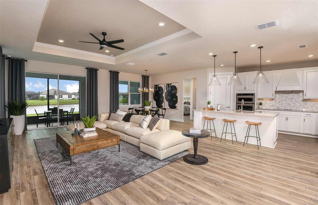 An open-concept living room and kitchen feature light wood flooring, a sectional sofa, and island seating — 11317 CLAY AVENUE, PARRISH, FL