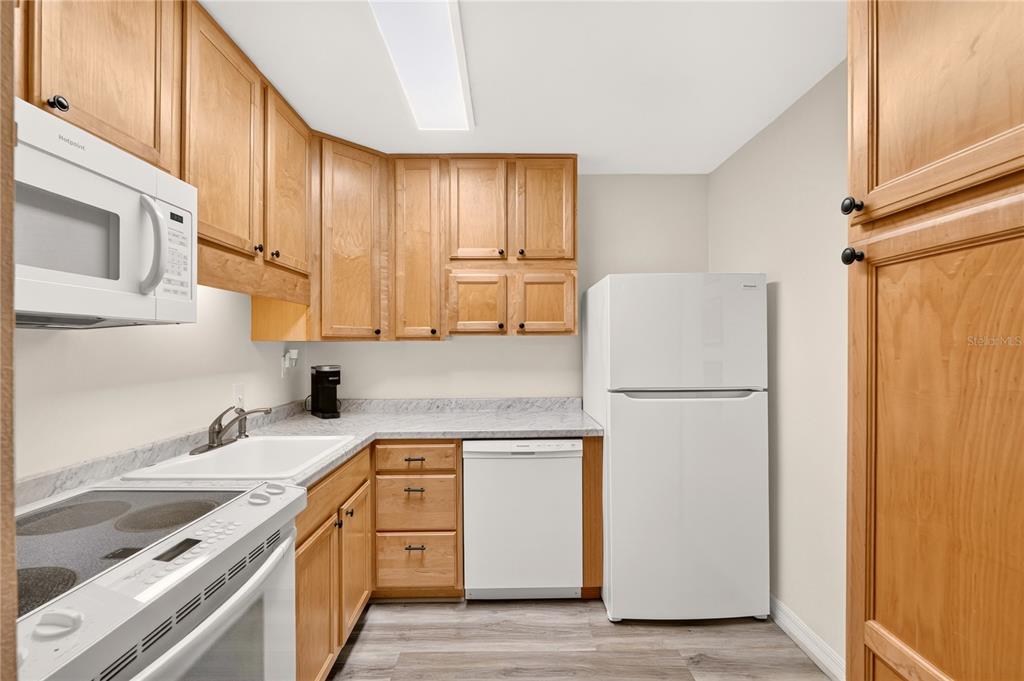 A kitchen features wood cabinets, white appliances, a laminate countertop, and light-colored flooring — 2842 SW 14TH DRIVE UNIT 103, GAINESVILLE, FL