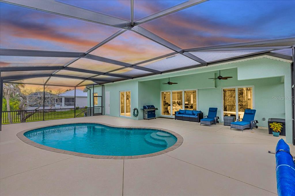 A swimming pool sits on a patio enclosed by a screened lanai behind a house — 16883 ACAPULCO ROAD, PUNTA GORDA, FL