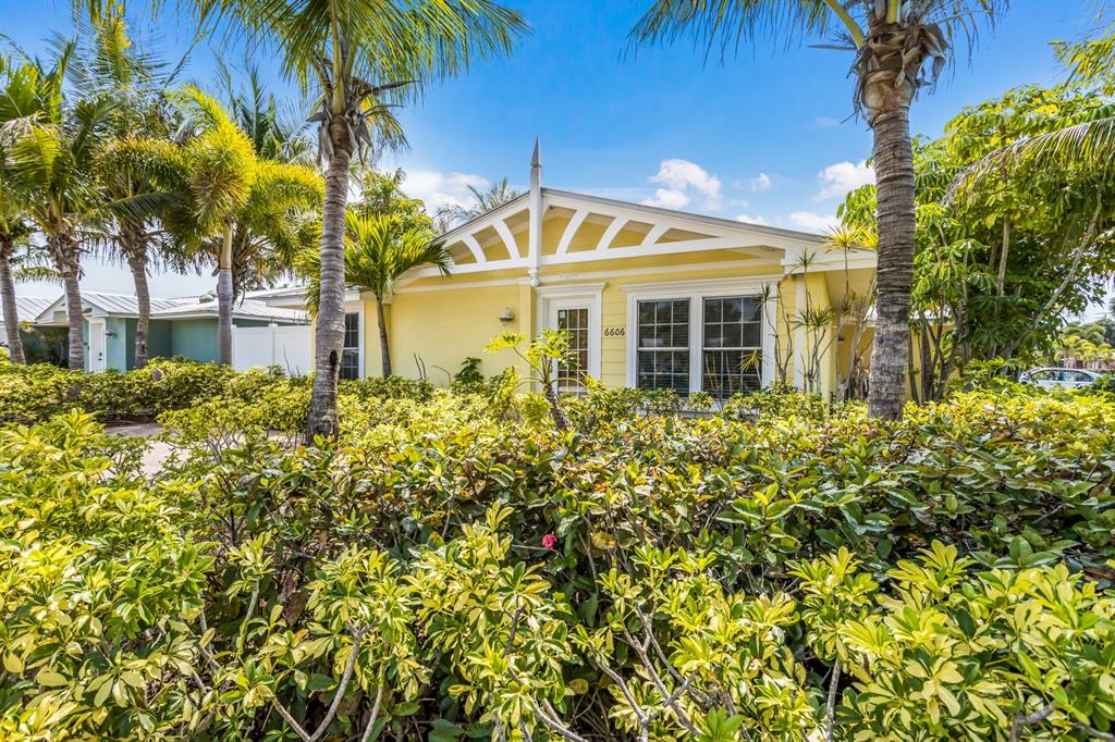 A yellow house with a white decorative gable is surrounded by lush tropical landscaping — 6606 HOLMES BOULEVARD UNIT 3, HOLMES BEACH, FL