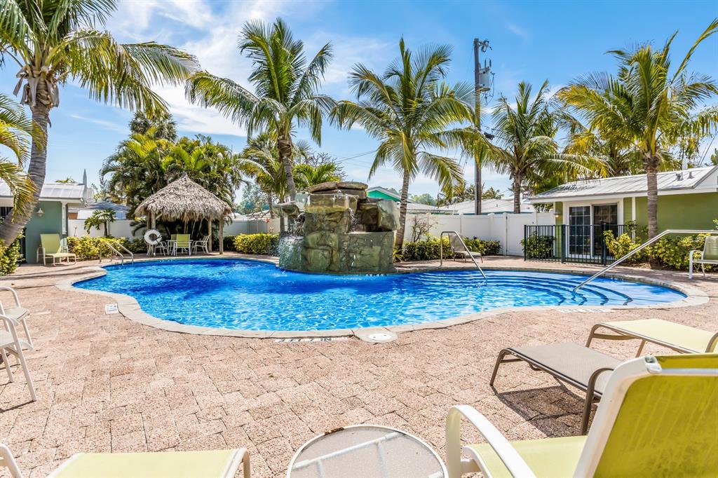 A swimming pool with a rock waterfall feature surrounded by lounge chairs and palm trees — 6606 HOLMES BOULEVARD UNIT 3, HOLMES BEACH, FL