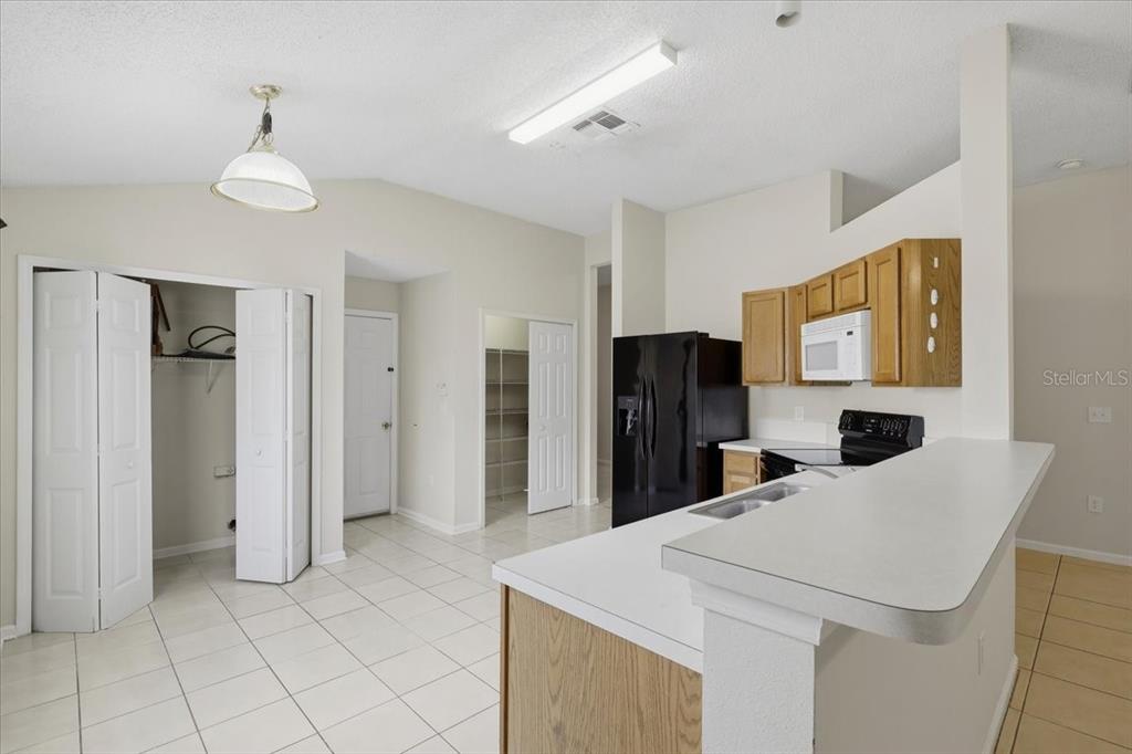 A kitchen with white countertops, light wood cabinets, black appliances, and tiled flooring — 3 LOUVET LANE, PALM COAST, FL