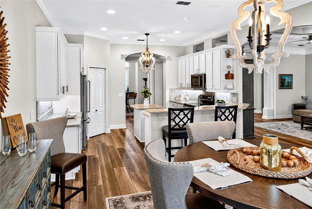 A kitchen and dining area feature white cabinetry, wood-look flooring, and two decorative chandeliers — 101 LONGVIEW WAY N, PALM COAST, FL