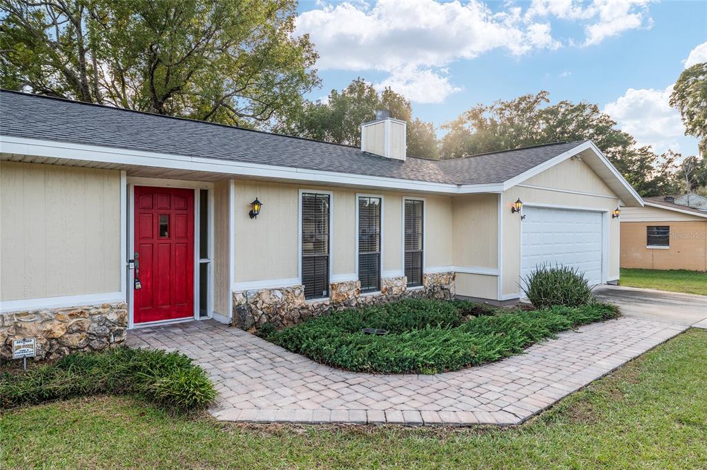 A single-story house with beige siding, a red front door, and a stone-accented foundation — 3300 SE 32ND STREET, OCALA, FL