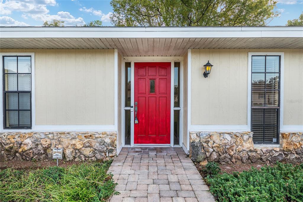 A red front door is centered between two windows on a house with stone siding — 3300 SE 32ND STREET, OCALA, FL