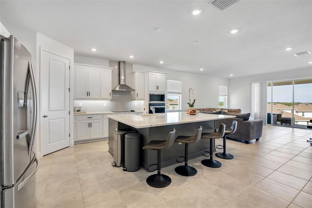 A modern kitchen features white cabinets, a dark gray island with barstools, and tile flooring — 2100 KEYSTONE CIRCLE, MINNEOLA, FL