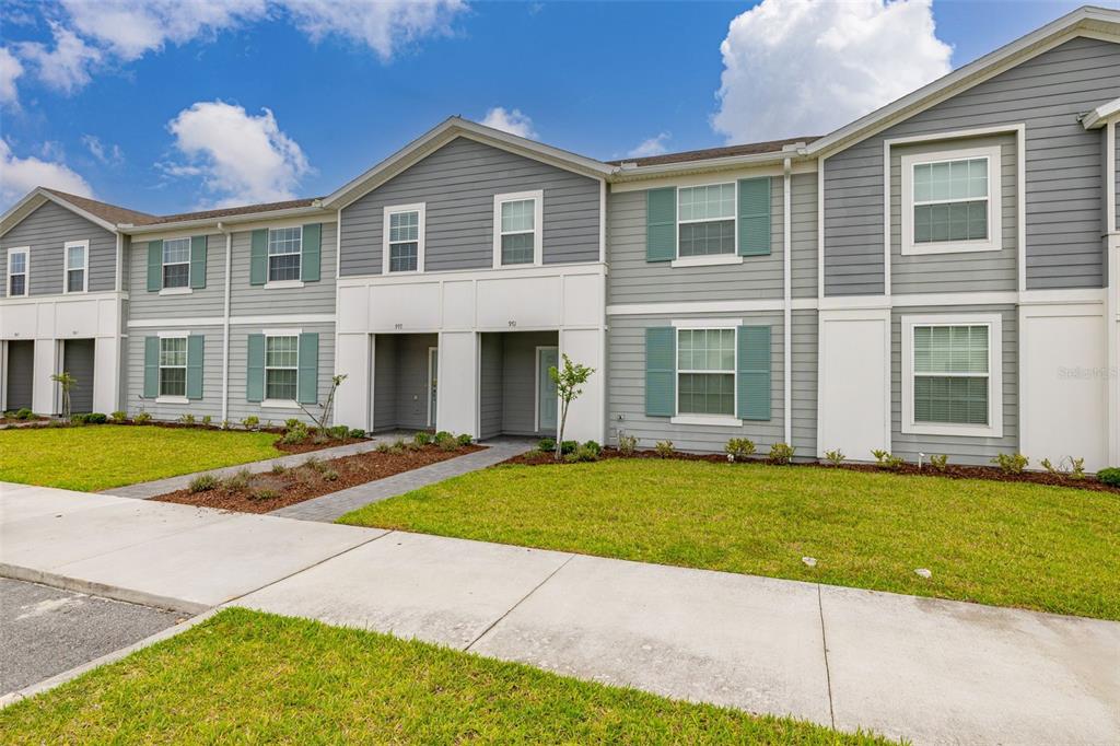 A two-story townhouse exterior with gray siding, white trim, and green shutters under a blue sky — 971 PARADISE DRIVE, DAVENPORT, FL