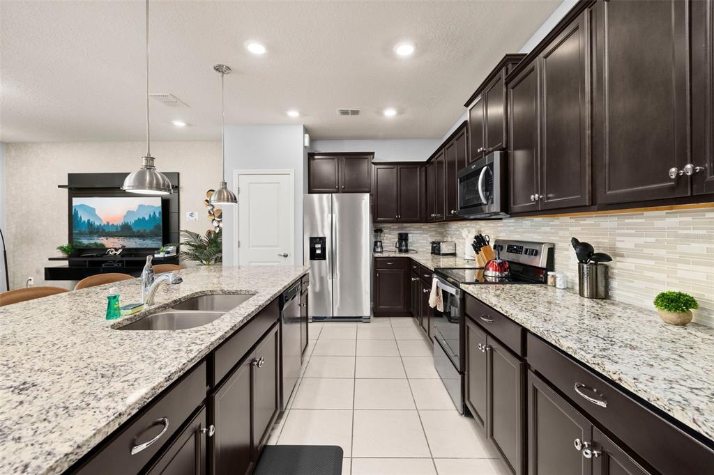A kitchen features dark wood cabinets, granite countertops, stainless steel appliances, and a large island — 971 PARADISE DRIVE, DAVENPORT, FL