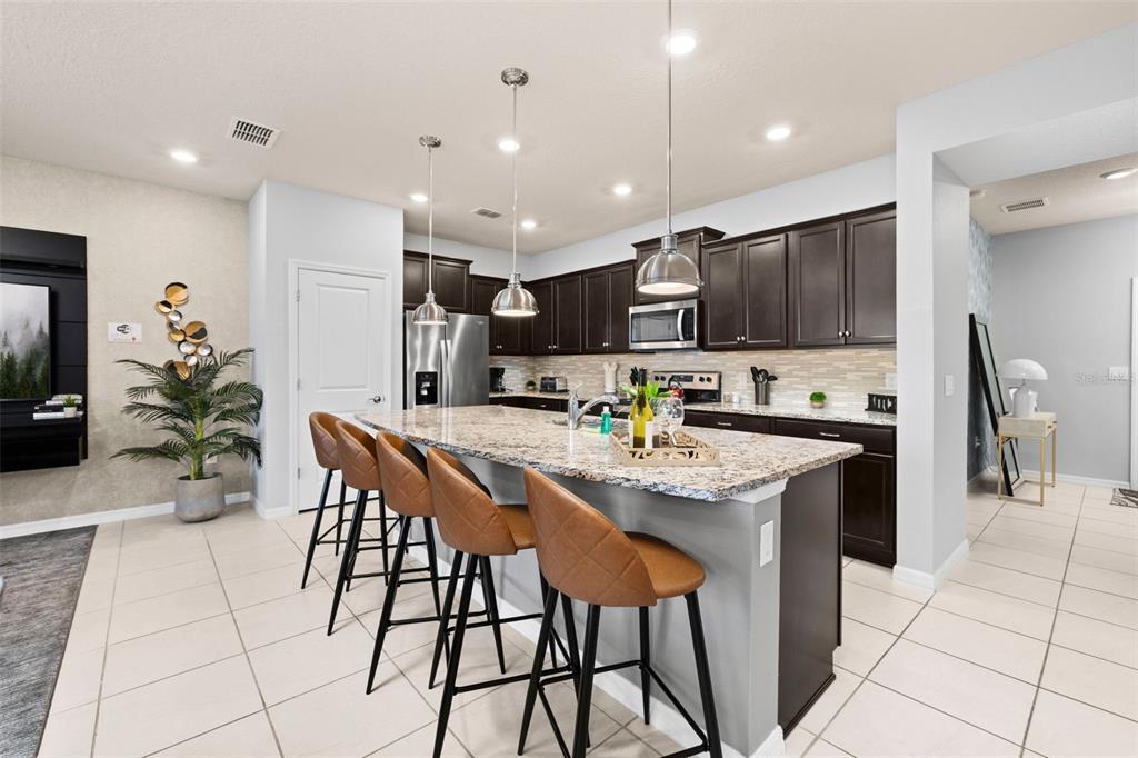 A kitchen features dark wood cabinets, granite countertops, a central island with barstools, and tile flooring — 971 PARADISE DRIVE, DAVENPORT, FL