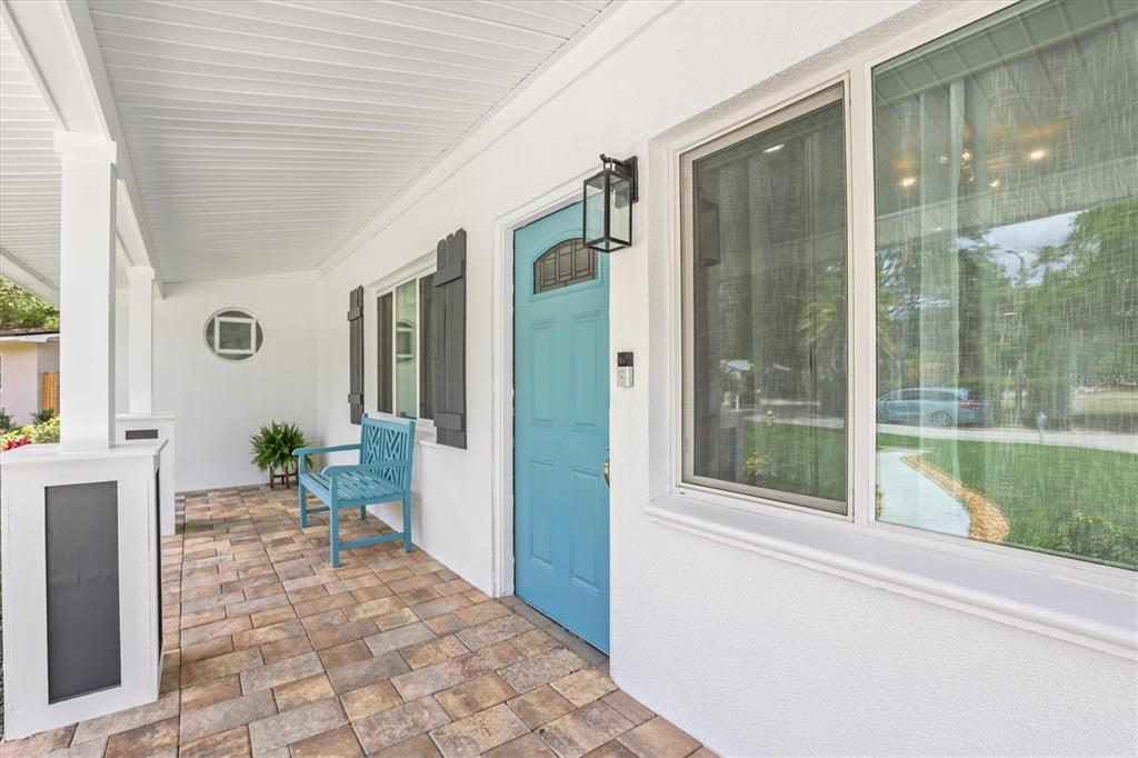 A covered front porch features a blue door, a matching bench, and paver flooring — 231 LIME CIRCLE S, DUNEDIN, FL