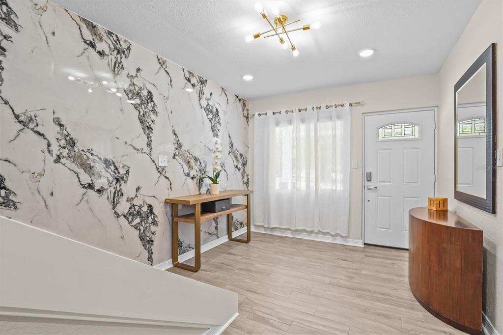 An entryway features a marble-patterned accent wall, a wood console table, and light wood flooring — 231 LIME CIRCLE S, DUNEDIN, FL