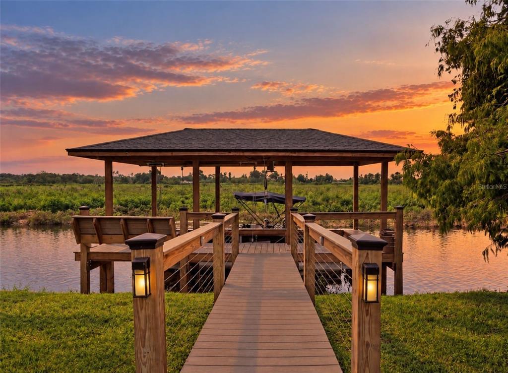 A wooden dock with a covered boat slip extends over a canal at sunset — 720 BAREFOOT BAY LOOP, GROVELAND, FL