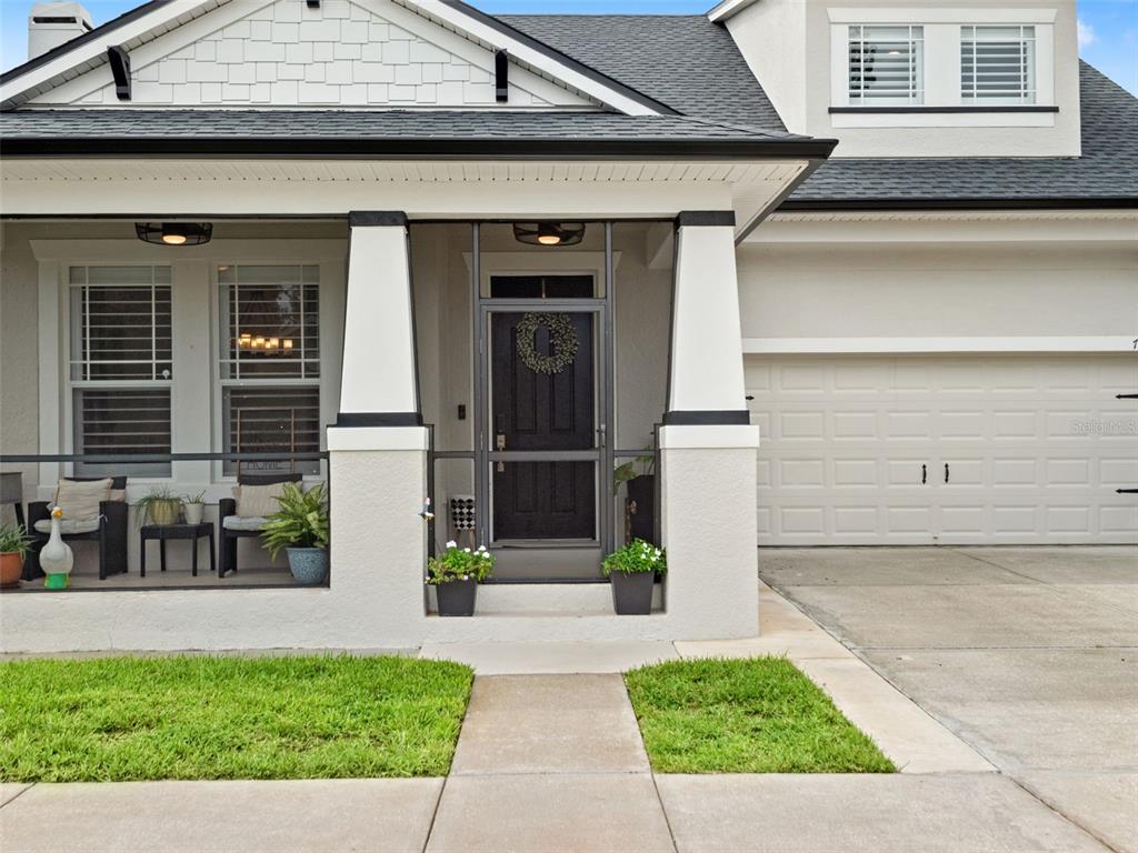 The exterior of a house features a covered front porch, a black door, and a garage — 720 BAREFOOT BAY LOOP, GROVELAND, FL