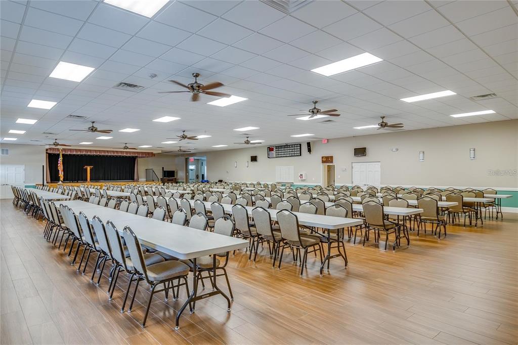 A large, open event hall features rows of tables and chairs, wood-look flooring, and ceiling fans — 5982 CORMORANT COURT, LAKELAND, FL