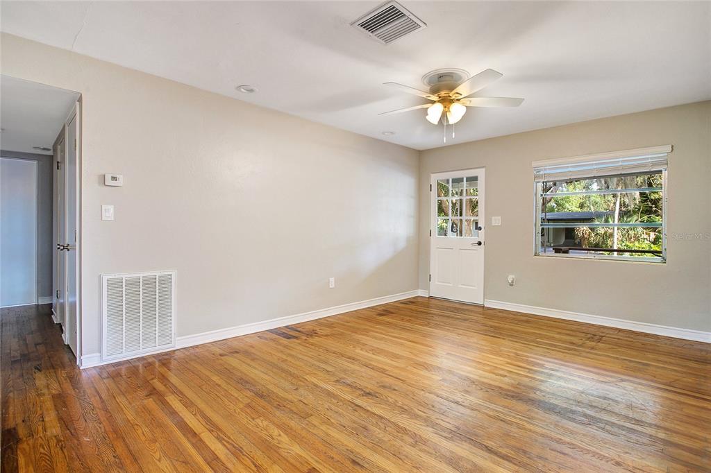 An empty living room features hardwood floors, a ceiling fan, a white door, and a window — 1955 ELAND AVENUE, WINTER PARK, FL