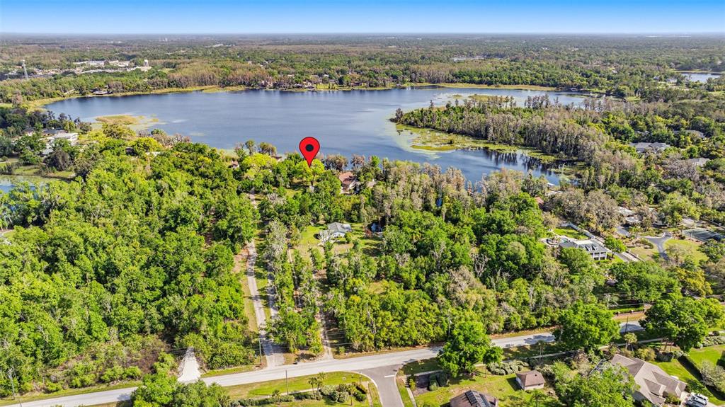 This aerial view shows a wooded property with a house located near a large lake — DEBUEL ROAD, LUTZ, FL