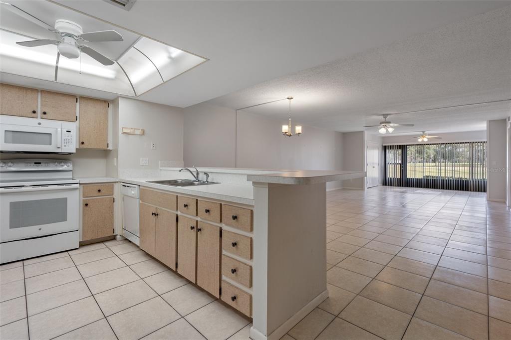 A kitchen with light-colored cabinets and tile flooring opens into a spacious living area — 3 CYPRESS RUN UNIT 35A, HOMOSASSA, FL